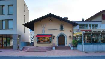 Vue extérieure de l'ancien cinéma Vaduz avec lettrage au-dessus de l'entrée et auvents rouges, situé entre deux bâtiments modernes.