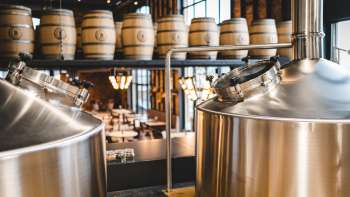 Vue d'une brasserie moderne avec des cuves en inox brillantes et des fûts en bois empilés en arrière-plan.