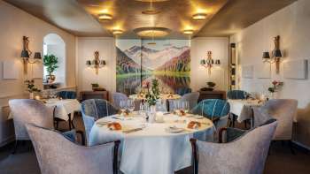 Une salle à manger élégante avec des tables dressées avec raffinement, une ambiance chic et une grande peinture représentant un paysage