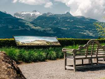 Banc en bois avec vue sur les Alpes et un panneau panoramique avec des noms de montagnes à Vaduz, Liechtenstein