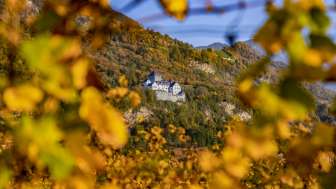 Vue du château de Vaduz au Liechtenstein en automne, encadré de feuilles dorées et d'un décor naturel automnal.