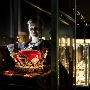 Une femme regarde le chapeau princier dans la Chambre du Trésor du Liechtenstein, entouré de vitrines éclairées.