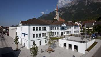 Le bâtiment Domus à Schaan avec sa façade blanche et sa vue sur l'église paroissiale - un centre culturel et un lieu de rencontre au cœur du Liechtenstein