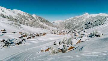 Vue aérienne de Malbun en hiver avec des maisons en bois enneigées, intégrées dans le paysage alpin du Liechtenstein.