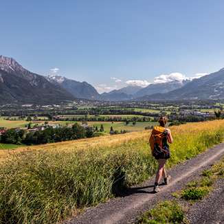 Une femme se promène sur un chemin de terre avec une vue panoramique sur la vallée du Rhin au Liechtenstein