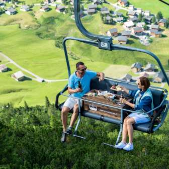 Deux personnes profitent d'un petit déjeuner montagnard dans le télésiège Genusssessel avec vue sur le village alpin de Malbun au Liechtenstein
