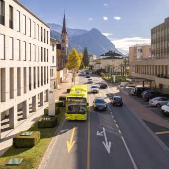 Un bus LIEmobil traverse Vaduz avec les Alpes en toile de fond et une architecture moderne.
