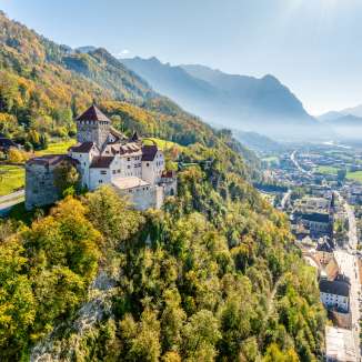 Vue du château de Vaduz au Liechtenstein avec des couleurs automnales, des montagnes et la vallée du Rhin en arrière-plan