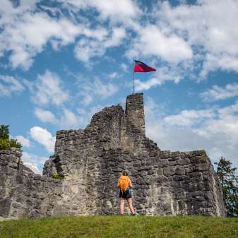 Randonneuse devant les ruines historiques du château de Schellenberg avec le drapeau du Liechtenstein flottant sous un ciel bleu