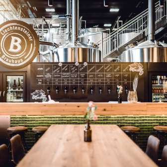 Vue intérieure de la Liechtensteiner Brauhaus avec des cuves de brassage brillantes, une installation de tirage moderne et un comptoir de dégustation confortable avec des tables en bois