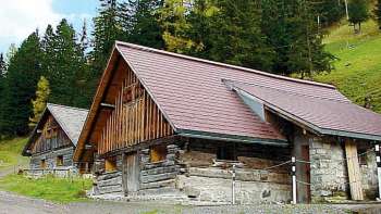Bâtiment historique en bois de l'ancien foyer de jeunes à Malbun devant un versant de montagne boisé.
