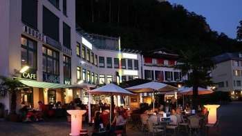Ambiance de soirée devant la Brasserie Burg à Vaduz avec terrasse illuminée et clients sous parasols.