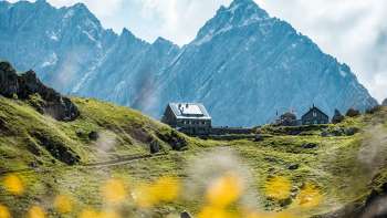 Vue sur le refuge Pfälzerhütte, situé sur un alpage verdoyant devant des parois rocheuses abruptes dans les Alpes liechtensteinoises.