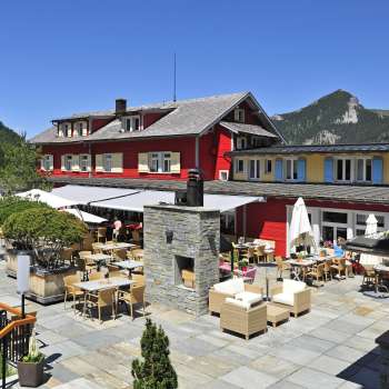 Vue extérieure du restaurant sous le soleil, avec une façade rouge et un panorama montagneux.