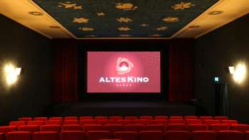 Salle de cinéma de l'Altes Kino Vaduz avec des sièges de cinéma rouges, une scène avec un rideau rouge et un plafond bleu avec des motifs d'étoiles dorées.