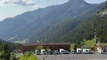Plusieurs camping-cars sont stationnés sur l'emplacement ensoleillé de Malbun, avec un panorama de montagnes en arrière-plan.