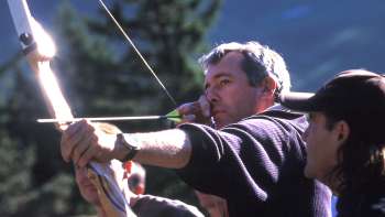Un homme se concentre sur la façon de tendre un arc lors d'une séance de tir à l'arc à Malbun, tandis qu'un guide se tient à ses côtés - une expérience de plein air passionnante au milieu des montagnes.
