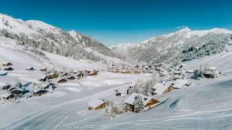 Vue aérienne de Malbun en hiver avec des maisons en bois enneigées, intégrées dans le paysage alpin du Liechtenstein.