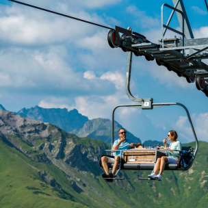 Deux personnes savourent un petit-déjeuner sur le télésiège Genus à Malbun, avec un impressionnant décor de montagnes en arrière-plan.