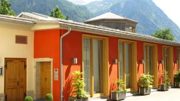 Vue extérieure du centre culturel Gasometer avec une façade colorée et un panorama alpin en arrière-plan.