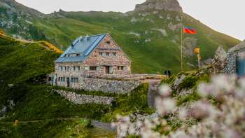 Gros plan sur le refuge Pfälzerhütte avec le drapeau du Liechtenstein dans une ambiance de soirée.