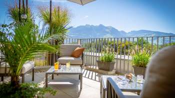 Terrasse ensoleillée avec meubles de salon modernes et panorama alpin en arrière-plan