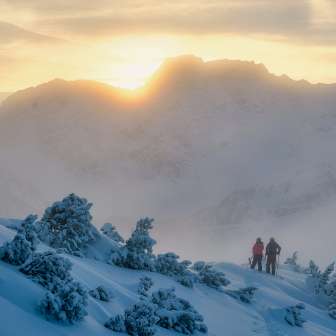 Deux personnes, dont Tina Weirather, marchent dans un paysage hivernal enneigé au coucher du soleil dans les montagnes du Liechtenstein.