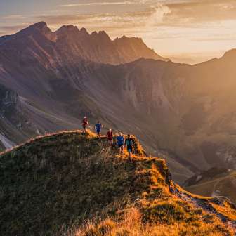Groupe de coureurs de trail sur une crête près de Malbun, Liechtenstein, dans la lumière chaude du coucher de soleil avec vue sur les Alpes.