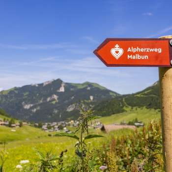 Panneau indicateur parcours du cœur alpin avec le village de montagne de Malbun en arrière-plan