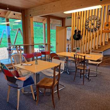 Salle de restaurant confortable avec des éléments en bois - La salle de restaurant est aménagée avec des meubles en bois clair et des guitares décoratives au mur, ambiance chaleureuse grâce à la lumière naturelle.