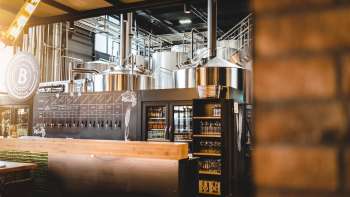 Vue intérieure d'une brasserie avec une installation de brassage en acier inoxydable et un comptoir de débit de boissons accueillant au premier plan.