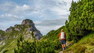 Randonneurs sur un sentier étroit à travers les pins de montagne à Malbun, Liechtenstein, avec vue sur des sommets rocheux