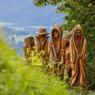 Vue détaillée de figures en bois sculptées dans une représentation mystique sur le sentier des légendes walser à Triesenberg, entouré d'une nature verdoyante