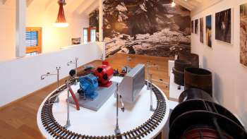 Modèle d'une turbine sur une plateforme d'exposition au musée Lawena, avec des photographies historiques en noir et blanc en arrière-plan.