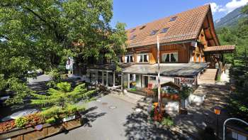 Vue extérieure de la maison principale du camping Mittagsspitze avec restaurant et terrasse ombragée.