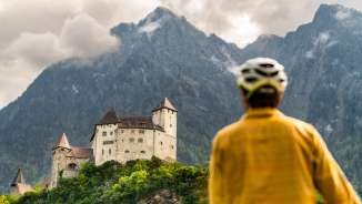 Un cycliste casqué contemple l'imposant château de Gutenberg sur fond de montagnes dramatiques à Balzers - Tour culturel à vélo au Liechtenstein