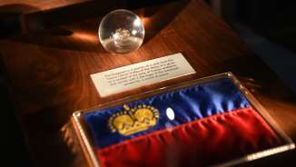 Pièce d'exposition dans le Trésor du Liechtenstein : drapeau du Liechtenstein avec couronne dorée et sphère en verre avec pièce historique trouvée