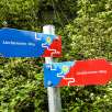 Panneau indicateur coloré du Liechtenstein-Weg avec des flèches rouges et bleues sur fond de forêt verte