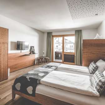 Chambre familiale confortable à l'hôtel Gorfion à Malbun avec des meubles en bois, un balcon et beaucoup de place pour des vacances détendues à la montagne.