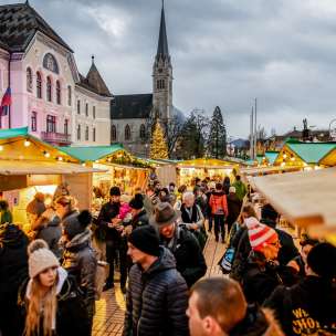 Photo d'ambiance du marché de Noël de Vaduz 2018 avec les stands de fête et la foule devant le bâtiment du gouvernement et la cathédrale.