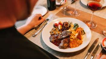 Détail d'un plat principal avec viande, légumes et sauces délicates, accompagné de vin rouge