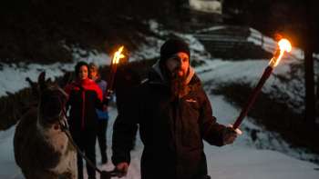 Personnes portant des torches lors d'un trekking avec des lamas et des alpagas sur un chemin enneigé dans l'obscurité