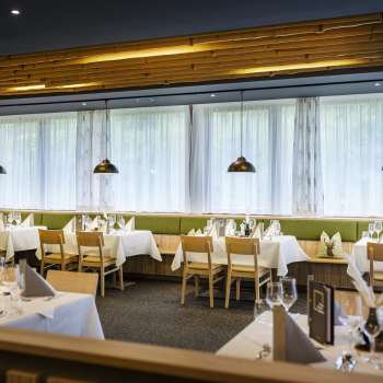 Une salle à manger accueillante avec des tables rondes et des chaises vertes moelleuses, décorée dans un style moderne et naturel.