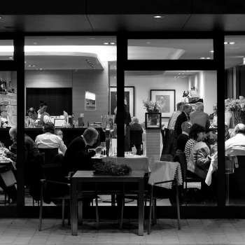 Photo en noir et blanc d'un restaurant animé avec vue de l'extérieur à travers la baie vitrée.