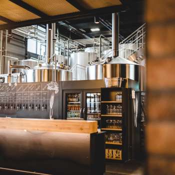 Vue intérieure d'une brasserie avec une installation de brassage en acier inoxydable et un comptoir de débit de boissons accueillant au premier plan.