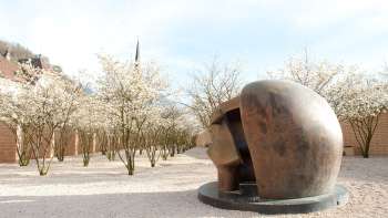 Sculpture en bronze "Figure in a Shelter" de Henry Moore dans le parc de sculptures de Vaduz - entourée d'arbres en fleurs au printemps.