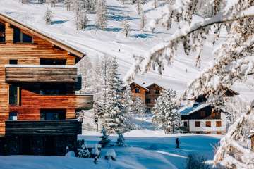 Chalets confortables dans la station de sports d'hiver de Malbun entourés d'arbres enneigés et de pistes de ski en arrière-plan