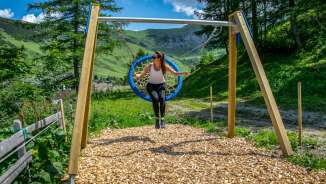 Une femme se balance sur une balançoire à Malbun, au Liechtenstein, entourée de montagnes, de prairies et de nature estivale.