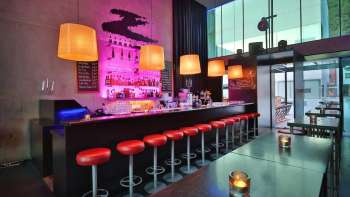 Bar moderne avec un long comptoir, des tabourets de bar rouges et un éclairage stylé rose et orange