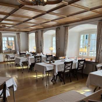 Salle de restaurant claire et classique avec des nappes blanches et un sol en bois.